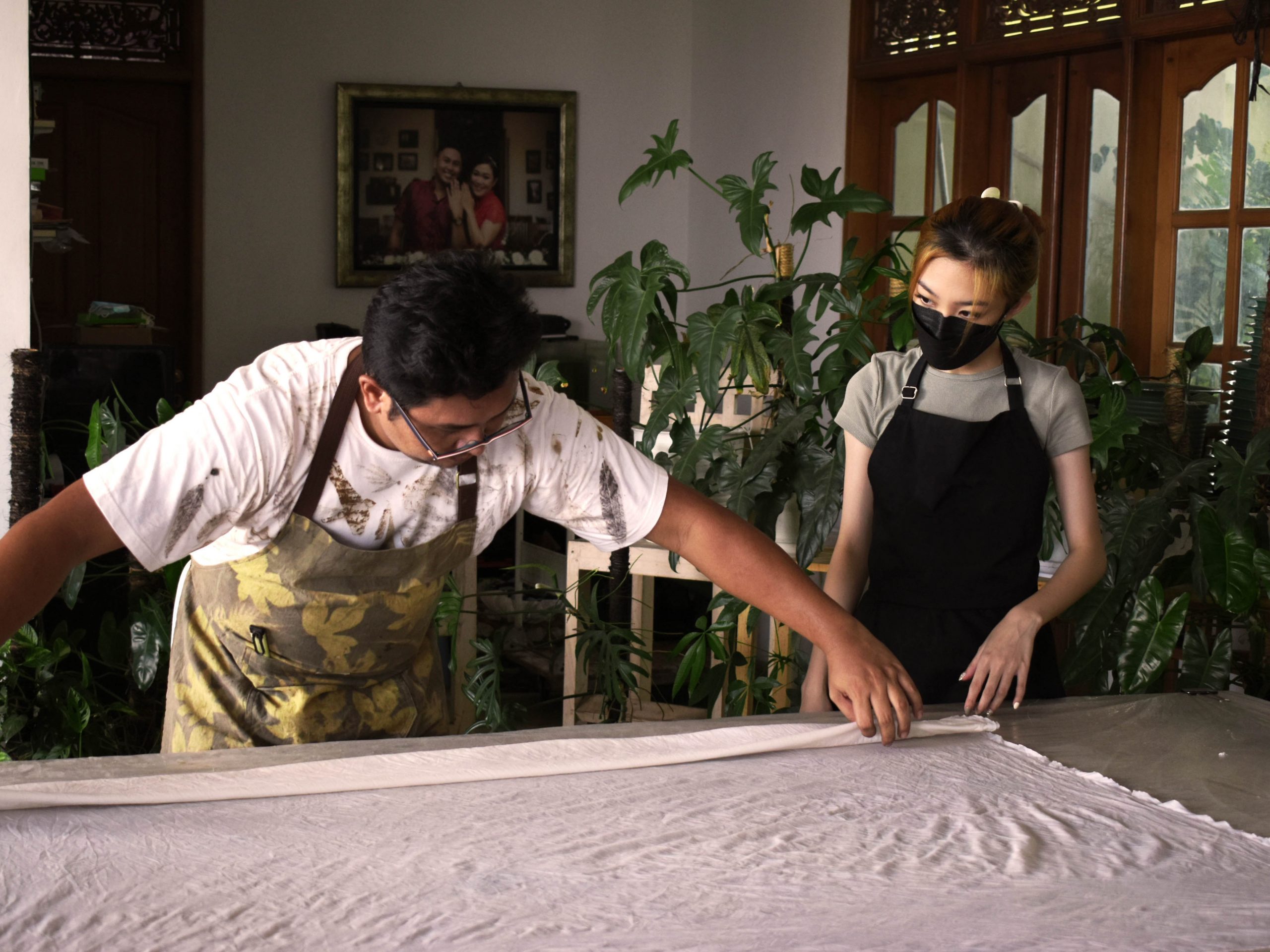 Two people working on eco printing fabric with plants in the background